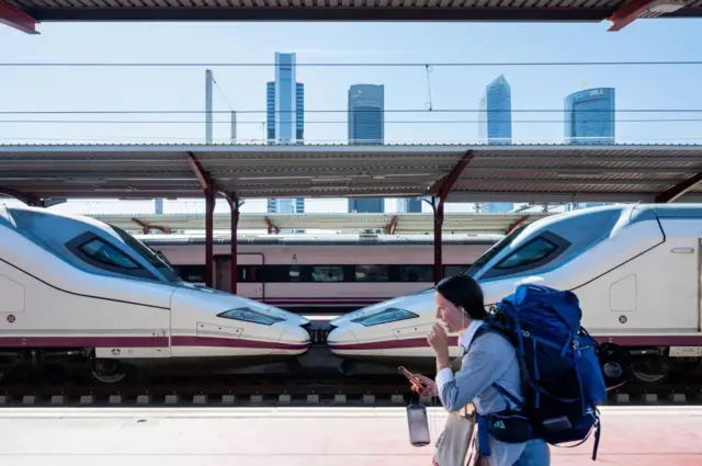 Una mujer con una mochila camina por el andén de una estación con un tren de alta velocidad estacionado.