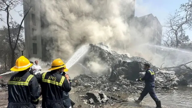 Bomberos con mangueras intentan controlar el incendio que dejó el avión al impactar pocos minutos después del despegue.