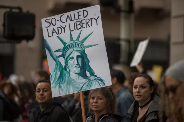 Una mujer con una pancarta en la que está dibujada la estatua de la libertad y dice: