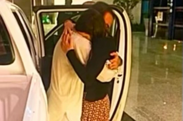 El momento en que Sammi y Safi se reencontraron a su regreso y se abrazaron: están de pie junto a la puerta abierta de un coche, Safi lleva un shalwar kameez tradicional blanco y Sammi lleva un shalwar kameez estampado.
