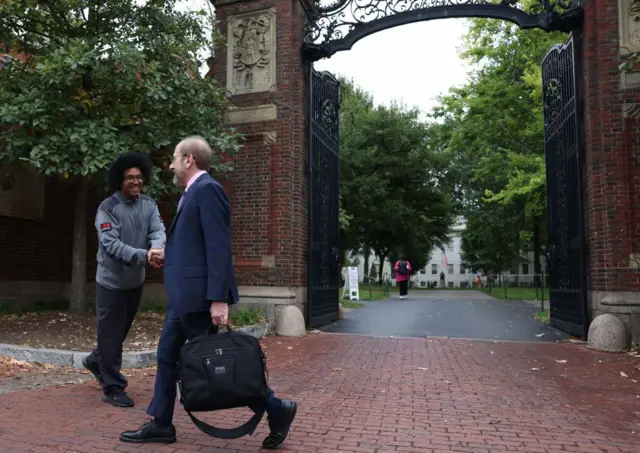 El presidente de Harvard, Alan Garber, saluda a un hombre en el portón del campus.
