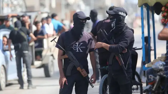 Dos combatientes, con ropas de civiles y fusiles colgando de sus hombros y los rostros cubiertos, charlan en una concurrida calle de Gaza.
