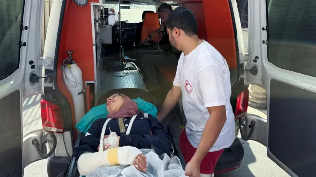 Una mujer con el brazo vendado es sacada en camilla de una ambulancia con la asistencia de un paramédico en Cisjordania