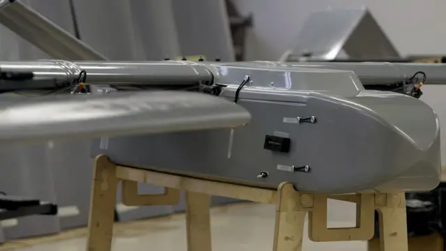 Un dron gris, con aspecto de avioneta, está colocado sobre una estructura de madera  
