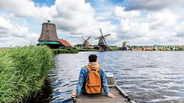 Hombre sentado en el muelle mirando los molinos de viento en Zaanse Schans, Zaandam, Países Bajos.