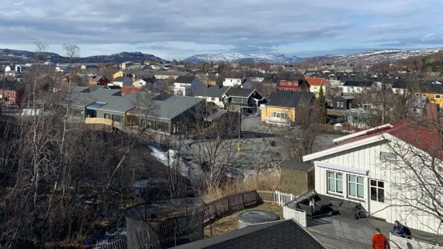 La ciudad de Kirkenes: varios edificios de una planta, calles y árboles, con colinas nevadas al fondo.