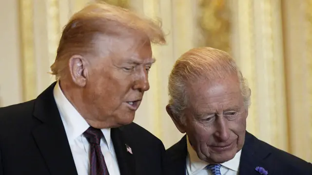 Donald Trump le comenta algo al rey Carlos III, ambos visten traje traje oscuro y miran hacia abajo