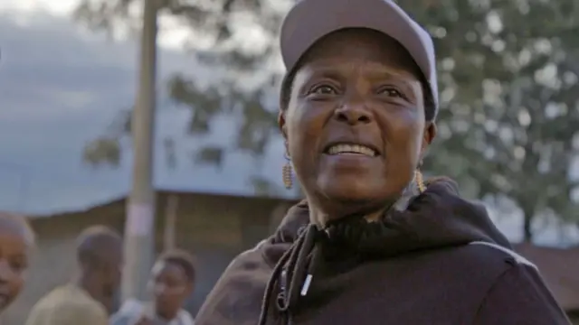 Baby Girl, vestida con una sudadera negra, una gorra blanca y pendientes de cuentas doradas, sonríe mientras reparte preservativos en una calle de Naivasha.