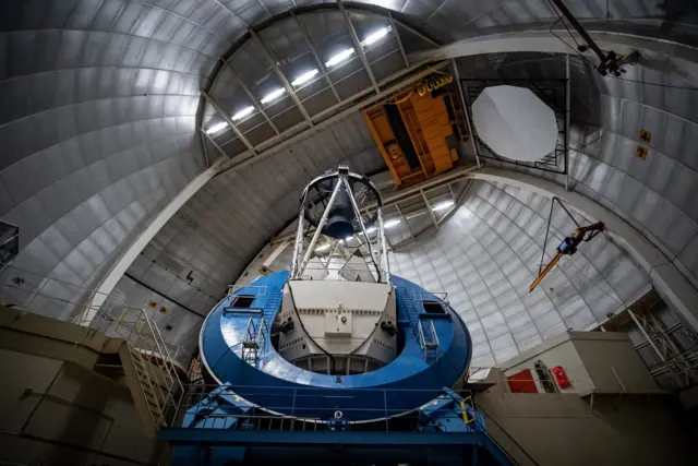 La foto muestra el interior de una enorme cúpula metálica, con paneles plateados curvados que se arquean en lo alto como el interior de una gigantesca carcasa de acero.