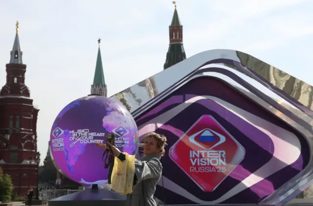 Una mujer se hace un selfi en la Plaza Roja de Moscú. Detrás de ella hay un gran globo decorativo y una pantalla con las palabras INTERVISION RUSSIA'25 y el eslogan 