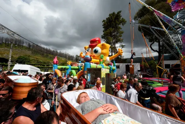 Personas llevan a hombros un féretro que pasa por delante de una atracción de feria de Bob Esponja.