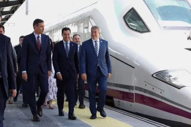 El presidente del gobierno español, Pedro Sánchez, (i) camina sonriente junto a un tren de alta velocidad estacionado con el presidente regional de Andalucía, Juanma Moreno (c) y otras autoridades en la inauguración del servicio AVE entre Madrid y Granada.