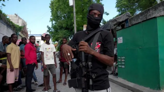 Un hombre con un rifle delante de otros hombres en un barrio de Puerto Príncipe