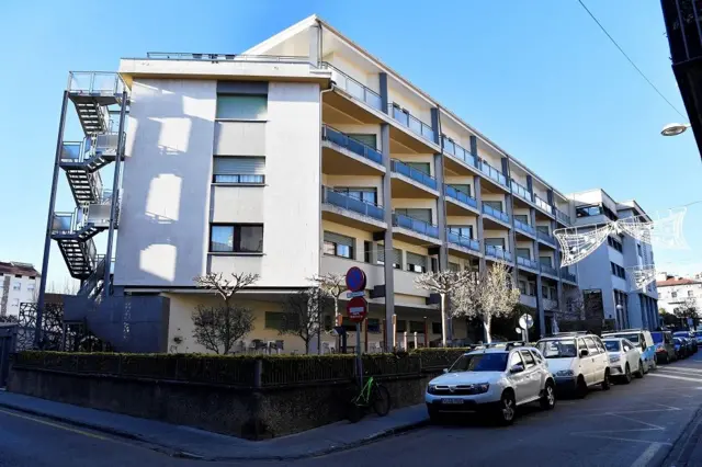 Vista externa de un edificio blanco de cuatro pisos con automóviles estacionados afuera