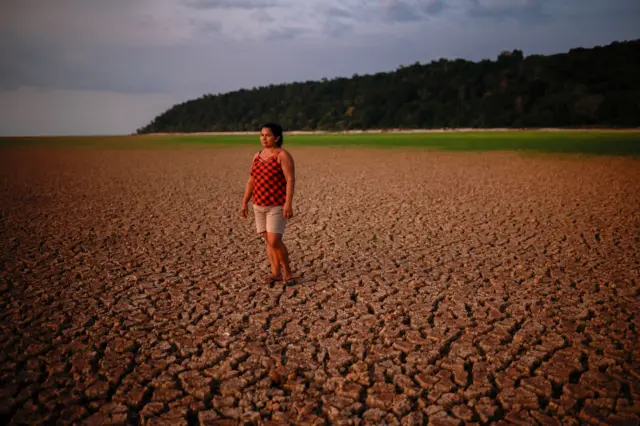 Una mujer parada en el lecho seco y resquebrajado de un río. 