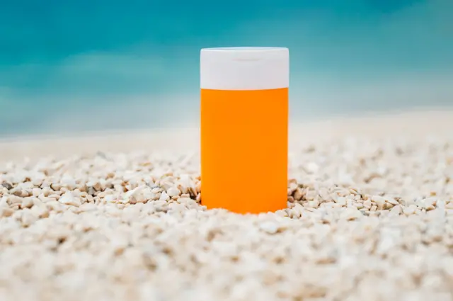 Un frasco de bloqueador solar en la arena de la playa.