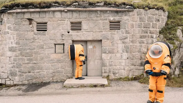 Dos estudiantes con trajes de astronauta naranjas en las montañas suizas.