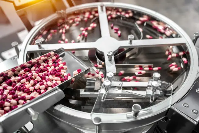 Cápsulas de color rojo y rosa son distribuidas a un surtidor en una fábrica farmacéutica