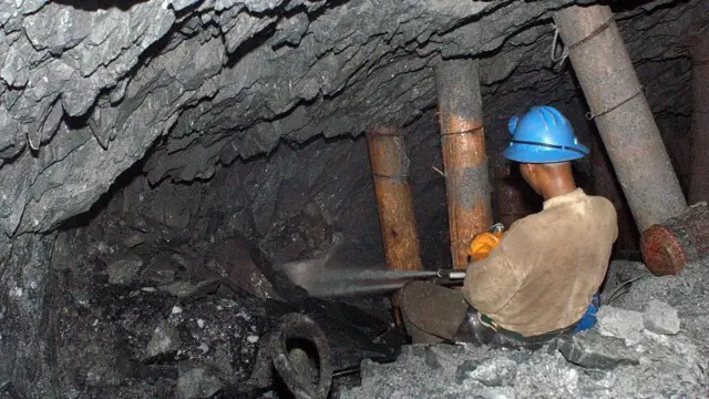 Un hombre con una camisa beige y un casco azul, de espaldas a la cámara, apunta un chorro de agua hacia una caverna rocosa dentro de una cueva.