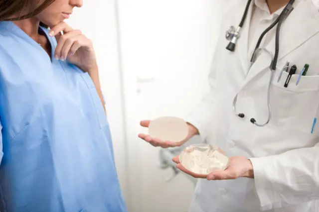 Una médica le muestra dos implantes mamarios a una paciente en una clínica