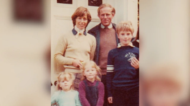 Una antigua foto familiar de Smyth, su esposa y sus tres hijos: dos hijas pequeñas y un hijo mayor. Posan delante de una puerta principal blanca y sonríen a la cámara.