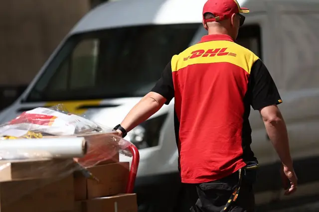 Un trabajador de DHL empujando un carrito con paquetes