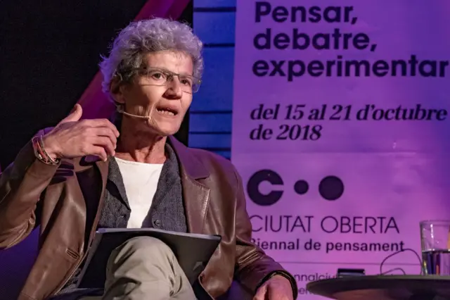 Josefina Birulés con lentes, una chaqueta marrón, sentada en una presentación pública
