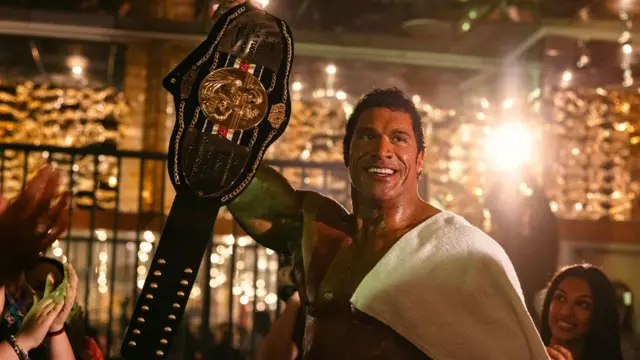 Dwayne Johnson como el luchador de la UFC Mark Kerr en The Smashing Machine, con una toalla sobre los hombros y rodeado de gente que aplaude.