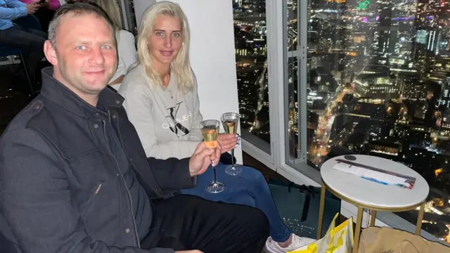 La pareja sentada en un bar con una copa de champagne y la vista de Londres de noche