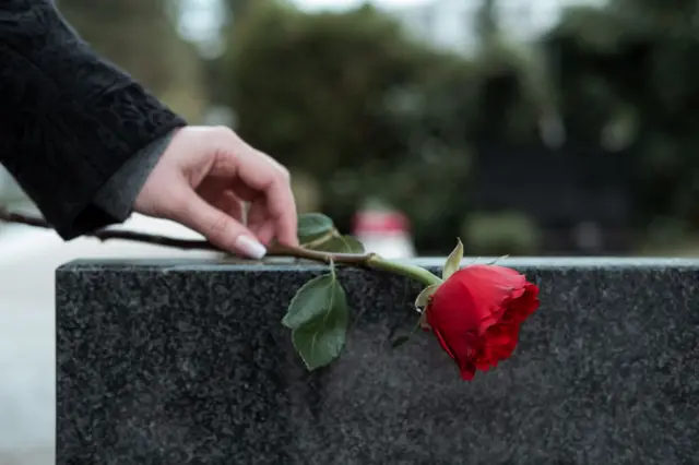 Una mujer coloca una flor sobre una tumba