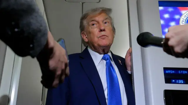 Trump luce corbata azul y asoma la cabeza por una puerta del Air Force One para hablar con los periodistas a su regreso de las reuniones del G7 en Canadá