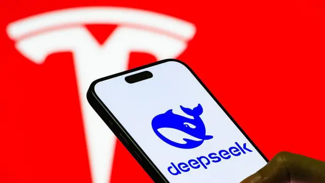 Una mano sostiene un teléfono en cuya pantalla se observa el logo de Deepseek mientras en el fondo se ve el logo de Tesla.