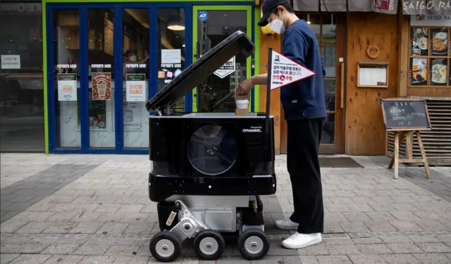 Un empleado de una cafetería coloca tazas de café en un robot de reparto de Robotis Co.