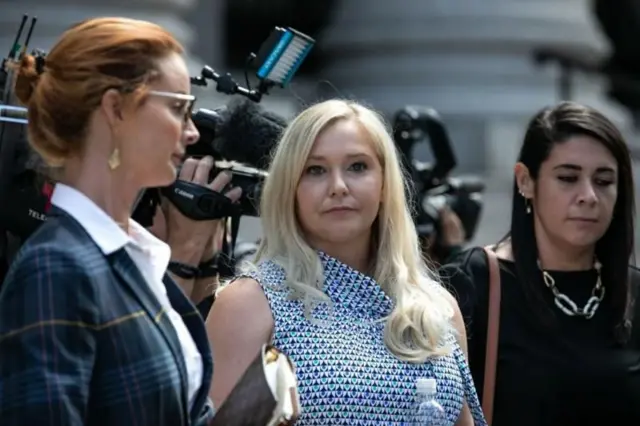Virginia Giuffre en el centro con un vestido azul y blanco con cámaras de los medios de comunicación detrás de ella y dos mujeres a cada lado