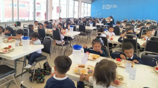 Niños en el comedor del colegio. Sentados en la mesa con bandejas enfrente. 