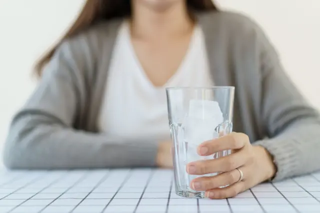Mujer con un vaso lleno de hielo en primer plano