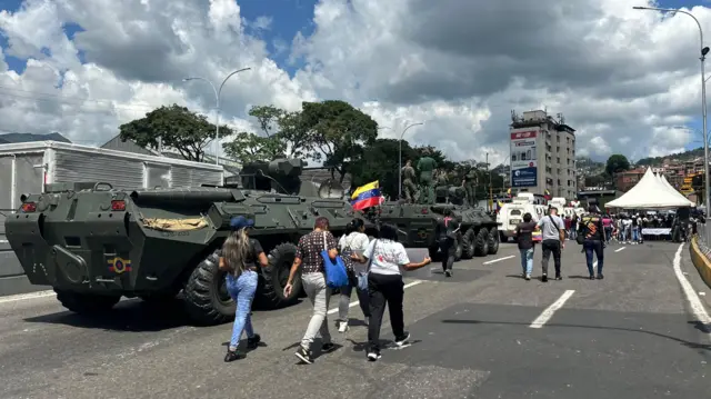 En una calle de Caracas, se desplazan tanques militares junto a personas vestidas de civil.