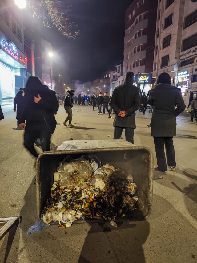 Manifestantes vestidos de negro en una calle. Lo que parecer ser un contenedor de basura se ve en el suelo
