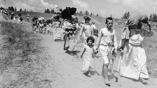 Niños y adultos palestinos marchan con sus posesiones tras ser desplazados de sus hogares en la Nakba en 1948