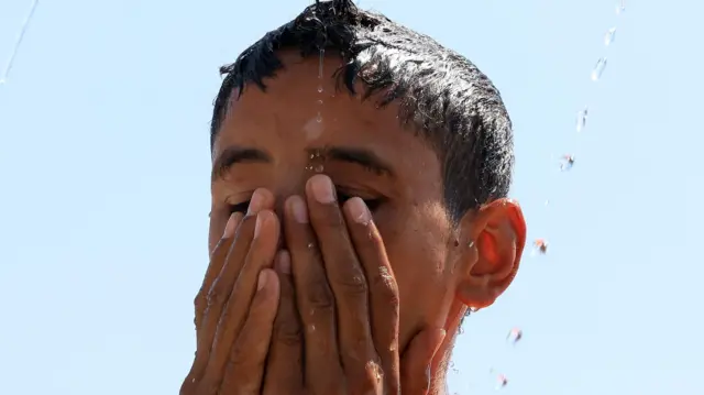 Niño con agua goteando sobre su cabeza en medio del clima cálido en Sana'a, Sanaa, Yemen - 15 de junio de 2025.