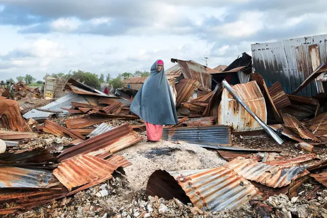 Una mujer sobre chapas rectangulares oxidadas de las que se suelen utilizar para construir viviendas precarias, en Awdheegle, Somalia. 