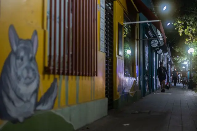 Personas caminan por la acera en un barrio de Santiago de Chile por la noche.