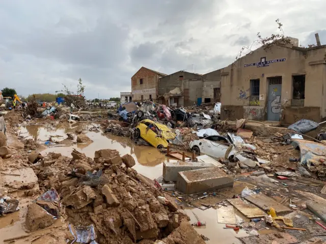 Una rambla llena de barro y coches destrozados.