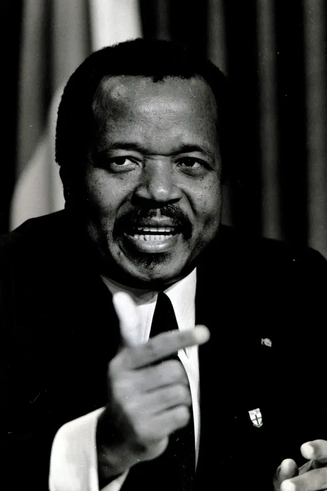 Fotografía en blanco y negro del presidente de Camerún, Paul Biya, de aspecto más joven, con traje y haciendo un gesto con la mano derecha.