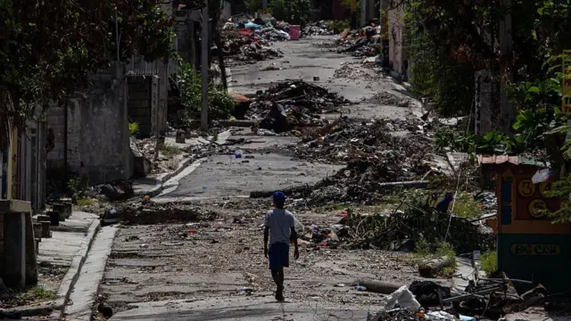 Un plano general de una figura solitaria caminando por una calle cubierta de escombros en el vecindario Delmas 30 en septiembre de 2025.
