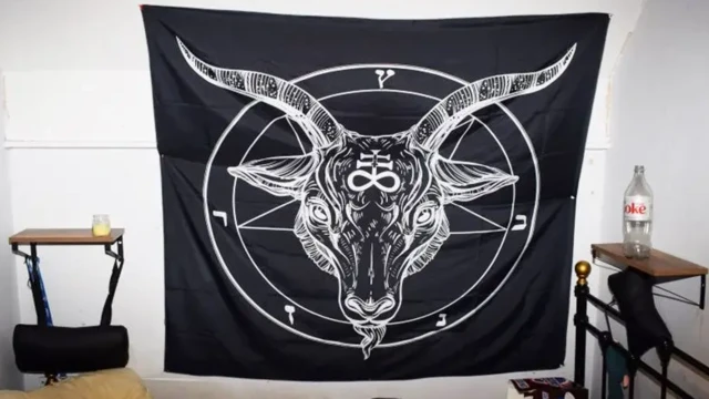 Un trozo de tela negra cuelga en una pared con una imagen satánica en blanco.