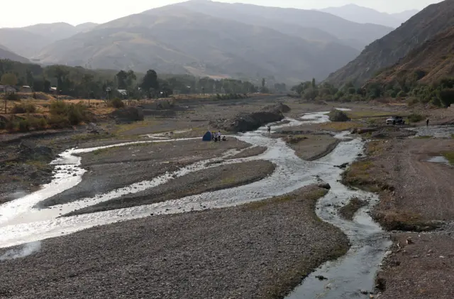 Iraníes hacen un picnic en un río casi seco, que alguna vez estuvo lleno, en el área de Fasham, al norte de Teherán, el 25 de agosto de 2025 - varias corrientes de agua corren por el lecho seco del río.