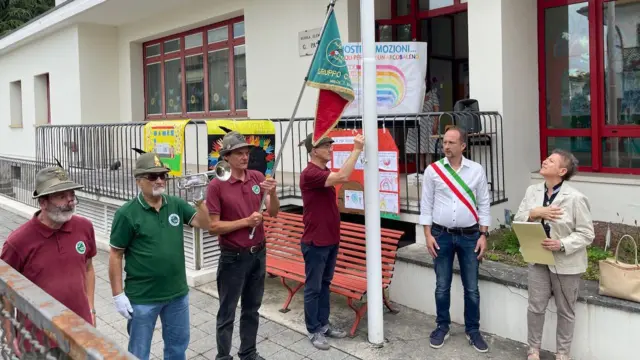 Ceremonia de clausura de una escuela; hombres con sombreros alpinos sostienen una bandera y tocan una corneta 