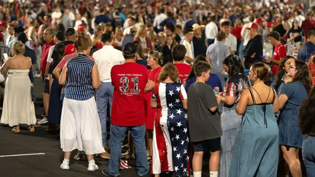 Un numeroso grupo de personas hace fila  para entrar en el  estadio State Farm en Glendale, Arizona, EE.UU. Una mujer tiene un vestido con la bandera de estrellas y franjas de Estados Unidos. Otro hombre  de  espaldas porta una camiseta roja con el número 31 que lee: 