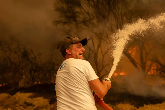 Un hombre lanza agua con una manguera en un incendio en Lamas, Galicia. 